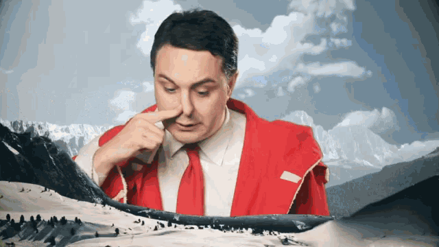 a man in a red jacket and tie holds his nose