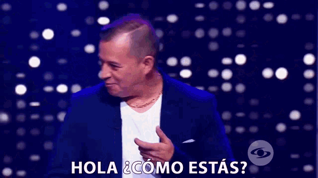 a man in a suit and white shirt is on a stage and says hola como estas
