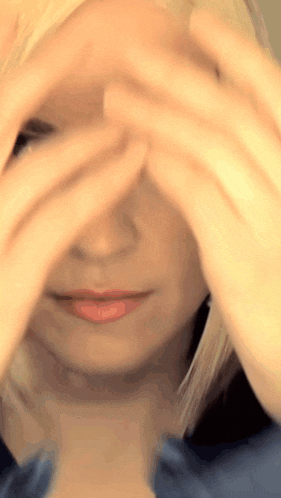 a woman covering her face with her hands and looking at the camera
