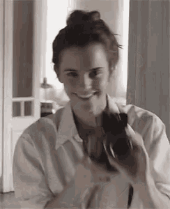 a woman in a white shirt is smiling while holding a camera in her hand .