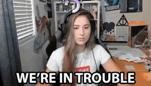a woman wearing headphones is sitting at a desk with the words `` we 're in trouble '' written above her .