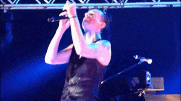 a woman singing into a microphone with a blue light behind her