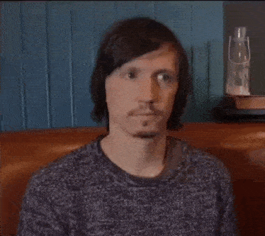 a man with long hair and a beard is sitting on a couch in front of a blue wall .