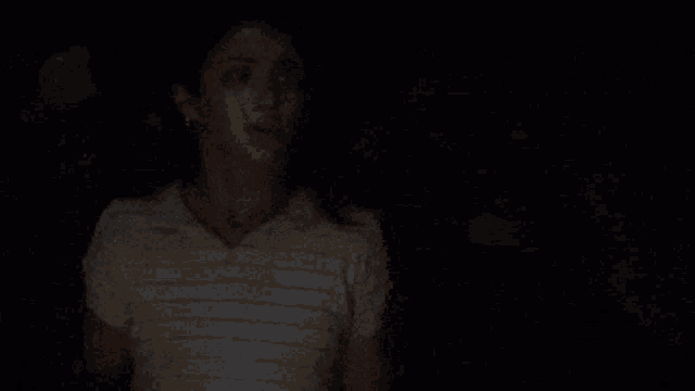 a woman in a striped shirt is standing in the dark looking at the camera .