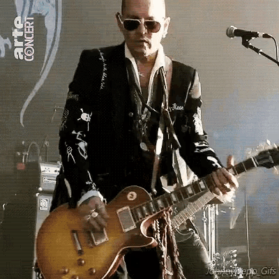 a man is playing a guitar and singing into a microphone while wearing sunglasses