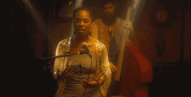a woman singing into a microphone with a man behind her playing a double bass