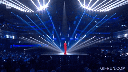 a woman in a red dress is standing on a stage in front of a crowd with a gifrun.com watermark