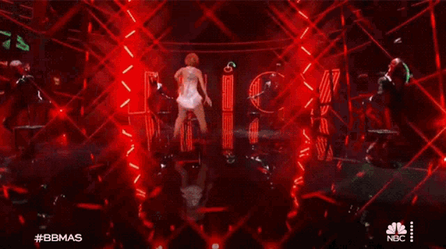 a woman in a white dress is dancing on a stage in front of a neon sign that says nbc