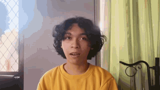 a young man with curly hair wearing a yellow sweater
