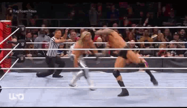 two wrestlers are fighting in a wrestling ring while a referee watches .