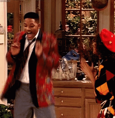 a man in a red jacket and tie is dancing with a woman in a red hat in a kitchen .