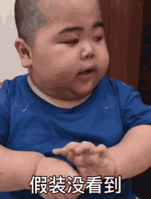a baby is wearing a blue shirt and making a funny face .