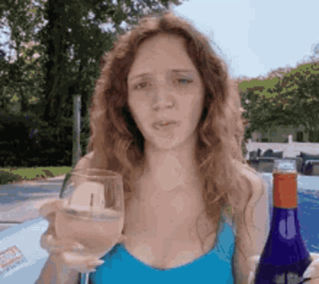 a woman in a blue tank top is holding a wine glass and a bottle of wine