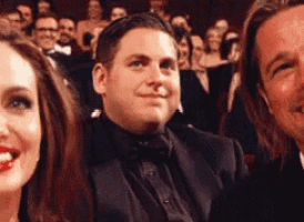 a man in a tuxedo and bow tie is smiling while sitting next to a woman .