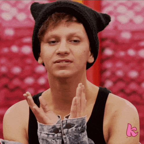 a man wearing a cat ear hat and a denim jacket has a pink k tattoo on his arm