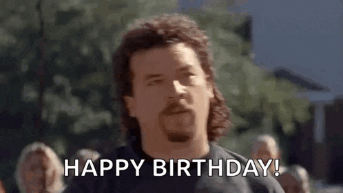 a man with a mullet and a beard is saying `` happy birthday '' .