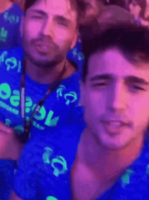 two men are standing next to each other in a crowd wearing blue shirts that say ' eee ' on them