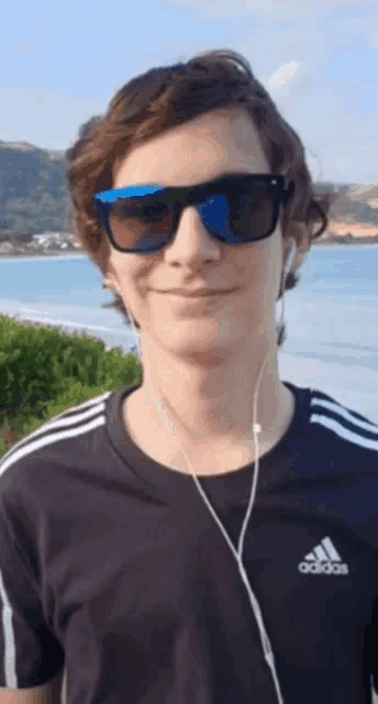 a young man wearing sunglasses and an adidas shirt smiles for the camera