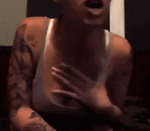 a woman with tattoos on her arms and chest is holding her chest with her hands .