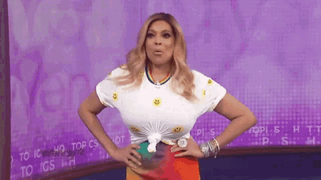 wendy williams is wearing a white shirt with smiley faces on it and a rainbow skirt .