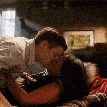 a man and a woman are kissing on a couch in a living room .