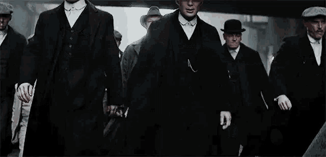 a group of men in suits and hats are walking down a street holding hands .