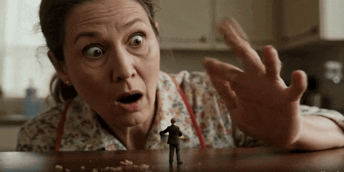 a woman with a surprised look on her face reaches out towards a small man on a table