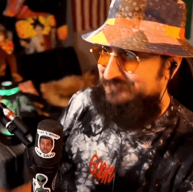 a man wearing a hat and sunglasses has a sticker on his shirt that says " what 's what the said " on it