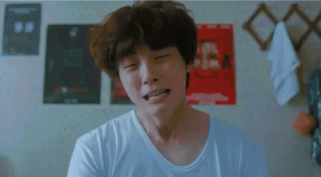 a young man is making a funny face in front of a wall with posters on it