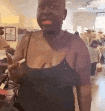 a bald woman in a black tank top is standing in a room holding a banana .