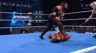 two men are wrestling in a wrestling ring with a referee in the background .