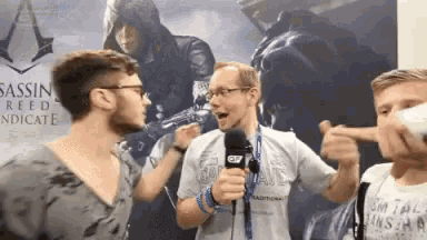 a man holding a microphone in front of a poster that says assassin 's creed