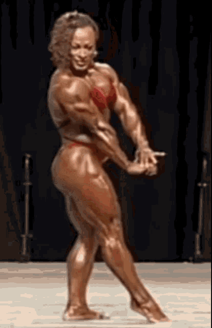 a very muscular woman in a bikini is standing on a stage in front of a black background .
