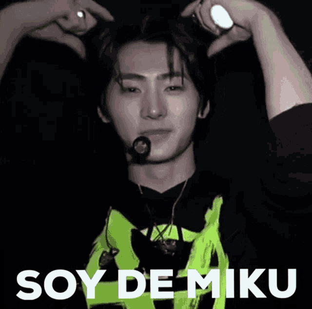 a man in a green shirt is holding a light stick in his hand and says soy de miku .