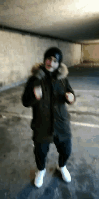a man wearing a mask and a black jacket is dancing in a parking garage