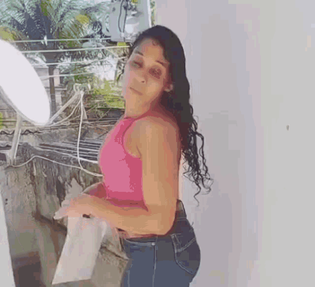 a woman in a pink tank top and jeans is standing next to a window .