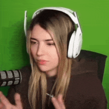 a woman wearing headphones and a brown hoodie is sitting in front of a green screen .