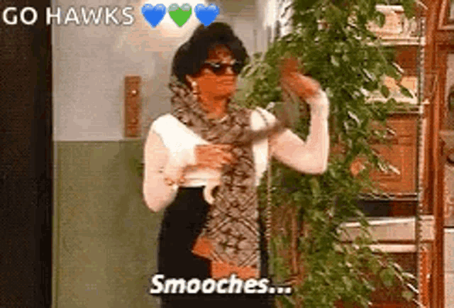a woman wearing sunglasses and a scarf is standing next to a plant and holding a snake .