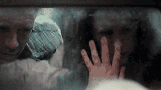 a woman 's hand is reaching out to touch a man 's face behind a window