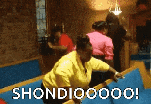 a woman in a yellow shirt is standing in front of a sign that says shondioooo