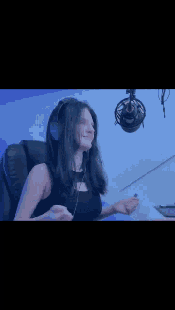 a woman wearing headphones is sitting in front of a microphone in a recording studio .