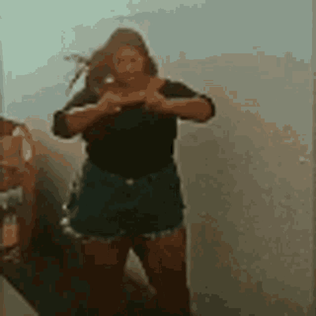 a woman in a black shirt and blue shorts is standing in front of a mirror .