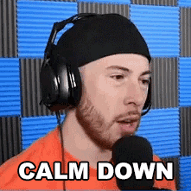 a man wearing headphones and a beanie is talking into a microphone and the words calm down are on the screen .