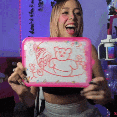 a woman is holding a pink board with a drawing of a teddy bear on it and laughing