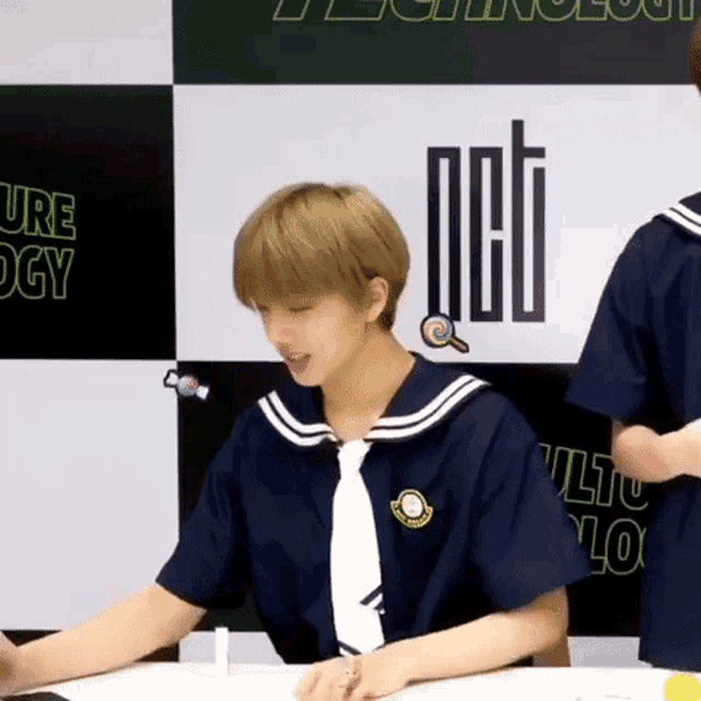 a young man in a sailor uniform is sitting at a table .