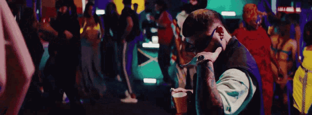 a man with a tattoo on his arm is holding a cup in front of a crowd