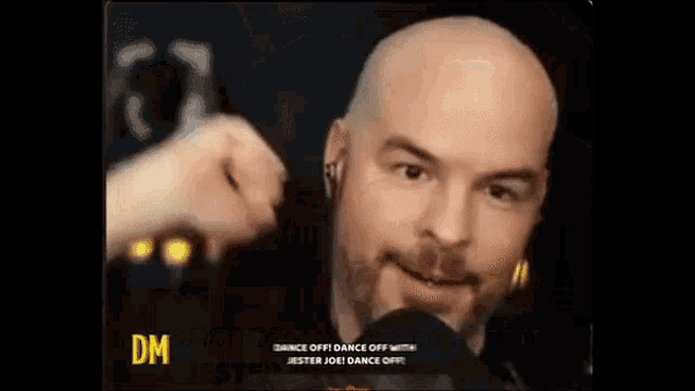 a bald man with a beard is talking into a microphone while wearing earbuds .