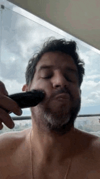 a man without a shirt is shaving his beard with a trimmer .