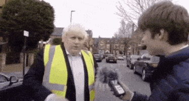 a man in a yellow vest is being interviewed by a young boy while holding a microphone .