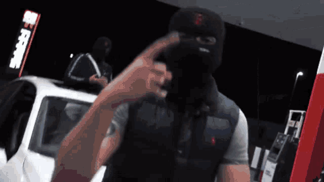 a man wearing a ski mask stands in front of a gas station